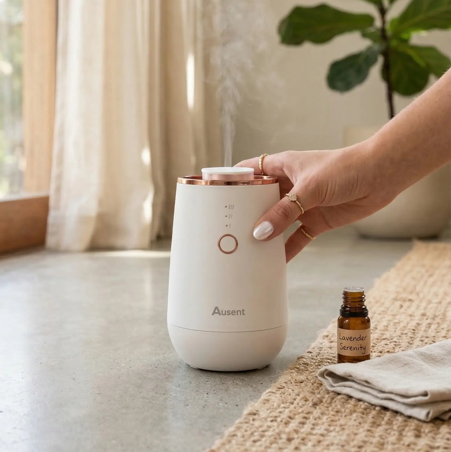 Hand holding a white Ausent diffuser with steam coming out, next to a bottle of essential oil on a textured surface.